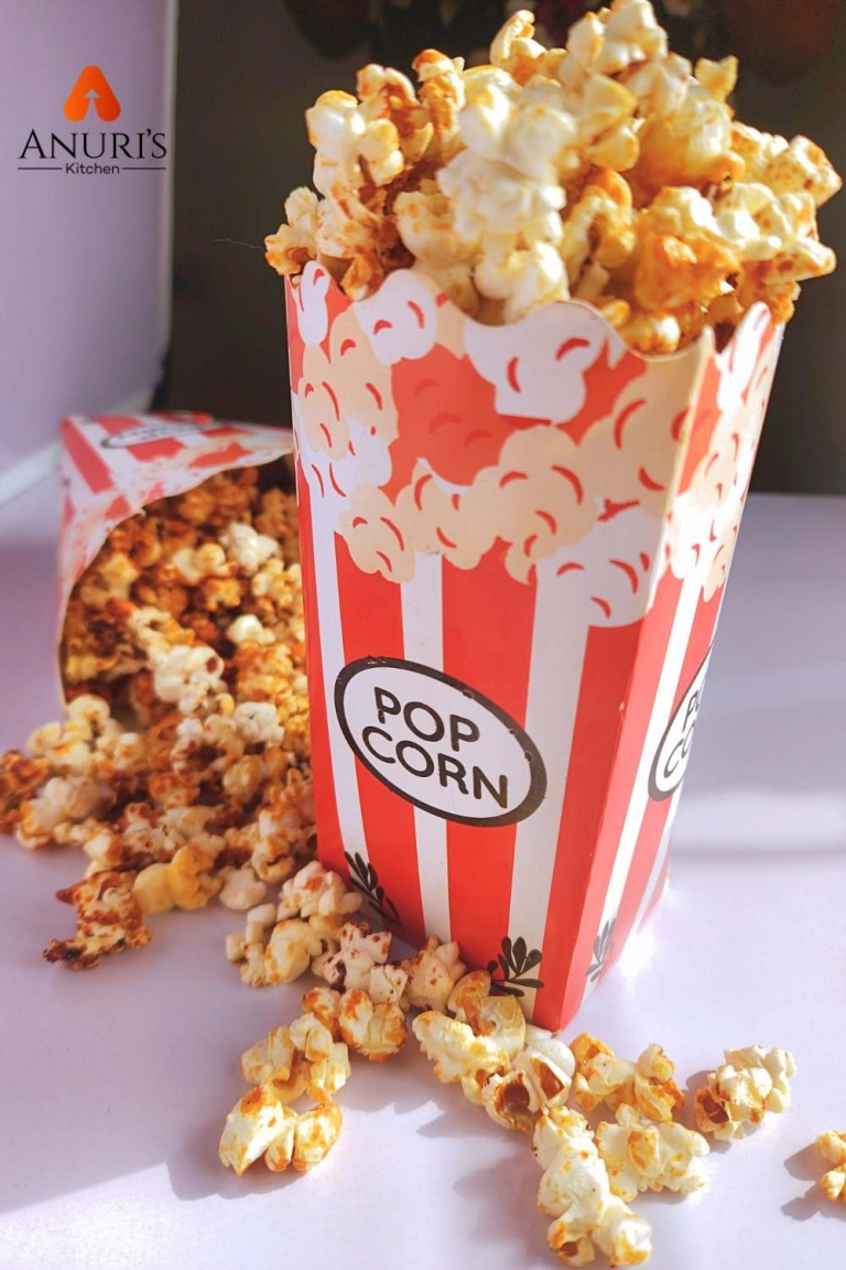 RED AND WHITE POPCORN CUP FILLED WITH BUTTERED POPCORN WITH A FEW KERNELS SCATTERED ON THE WOODEN TABLE.